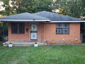 A single-story brick house with a gabled roof, a front door with a decorative glass panel, and a small porch area. - The Southern Spot (Baton Rouge)
