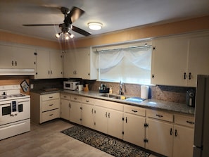 Une cuisine avec des meubles blancs, un four à micro-ondes, une cuisinière et un ventilateur de plafond.