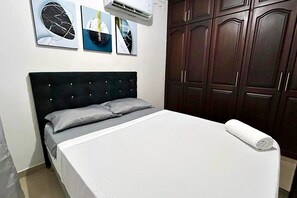 A bedroom with a bed, a headboard, a wall-mounted air conditioner, and a set of wooden cabinets. - El Caney Living (Cali)