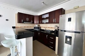 A kitchen with dark wooden cabinets, a stainless steel refrigerator, a microwave, and a gas stove. - El Caney Living (Cali)