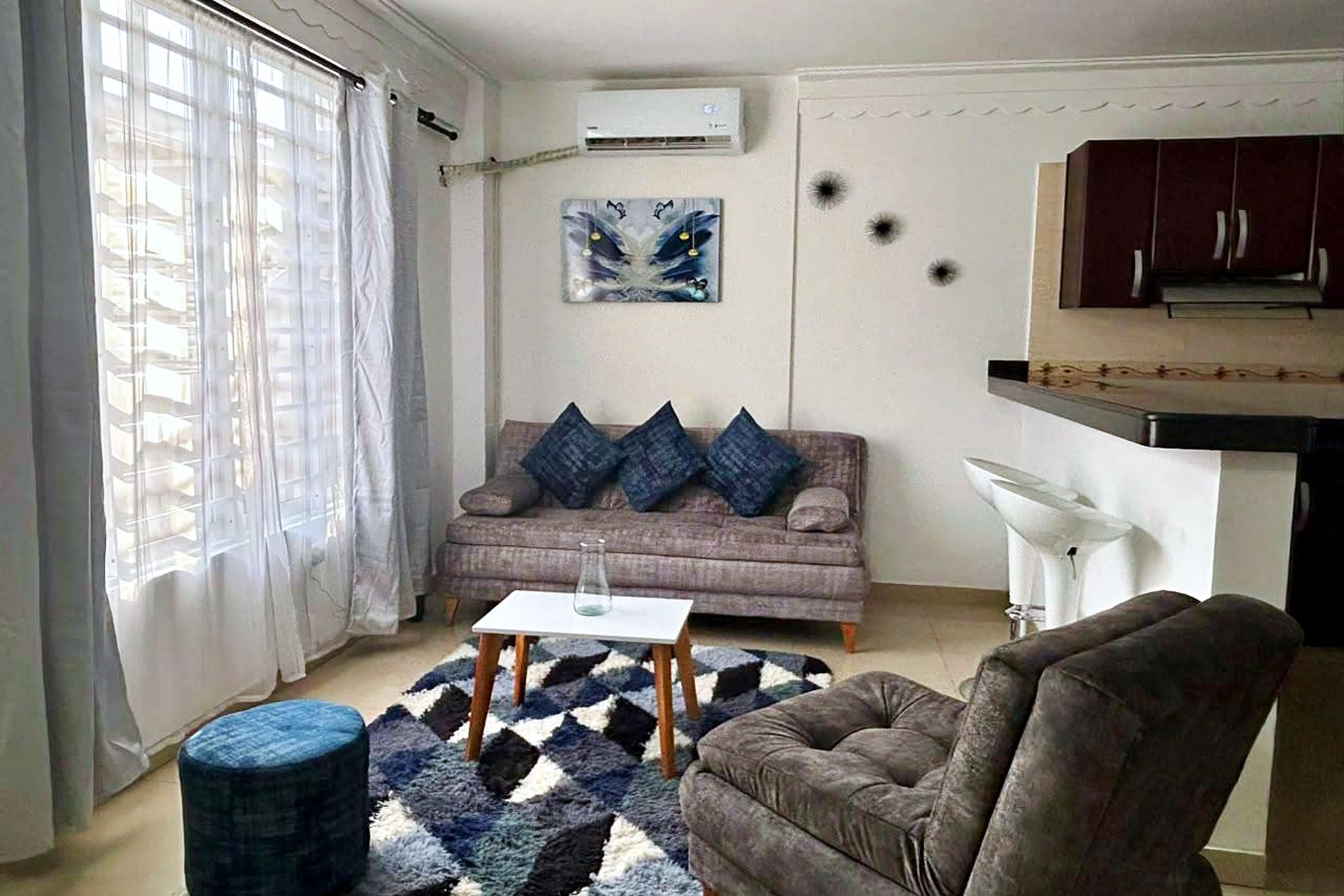 Una sala de estar con un sofá, una mesa de centro, una silla, un tapete y un cuadro en la pared.