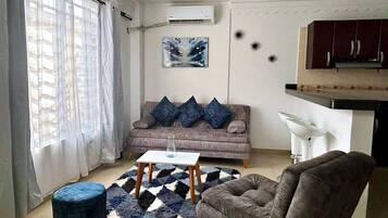 Una sala de estar con un sofá, una mesa de centro, una silla, un tapete y un cuadro en la pared.