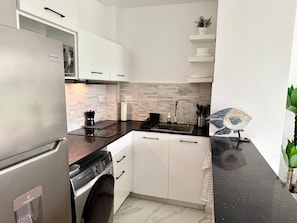 A compact kitchen with white cabinets, a stainless steel refrigerator, a washing machine, and a black countertop. - Paradise in Punta Cana (Higuey)