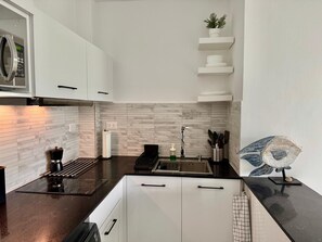A modern kitchen with white cabinets, a black countertop, a stainless steel range hood, and a hanging plant. - Paradise in Punta Cana (Higuey)