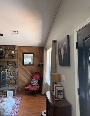 Una sala de estar acogedora con pared de piedra, un sillón rojo, una chimenea y una estantería.