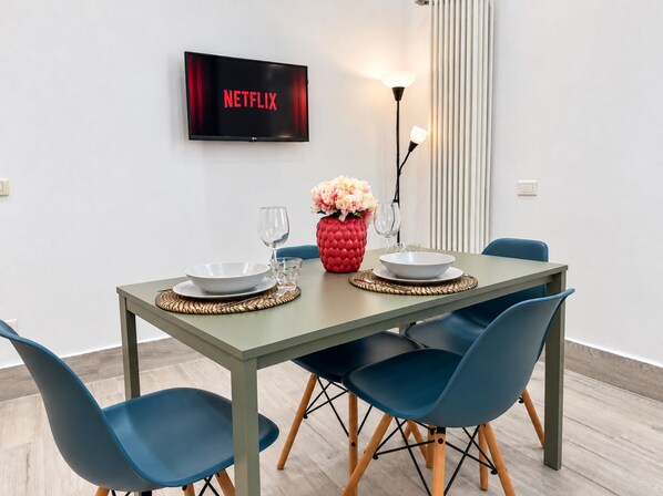 A dining area with a table set for two, a television displaying the Netflix logo, and a modern floor lamp. - New Listing (Cascina)