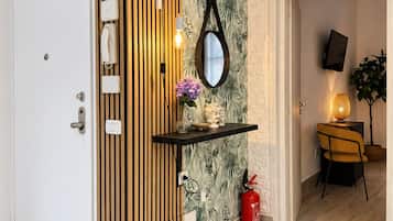 A modern interior with a wooden panel wall, a mirror, a shelf with decorative items, a fire extinguisher, and a television mounted on the wall.