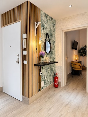 A modern interior with a wooden panel wall, a mirror, a shelf with decorative items, a fire extinguisher, and a television mounted on the wall. - New Listing (Cascina)