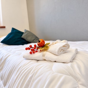 A neatly made bed with white bedding, a folded white towel, and decorative red berries and leaves. - New Listing (Cascina)