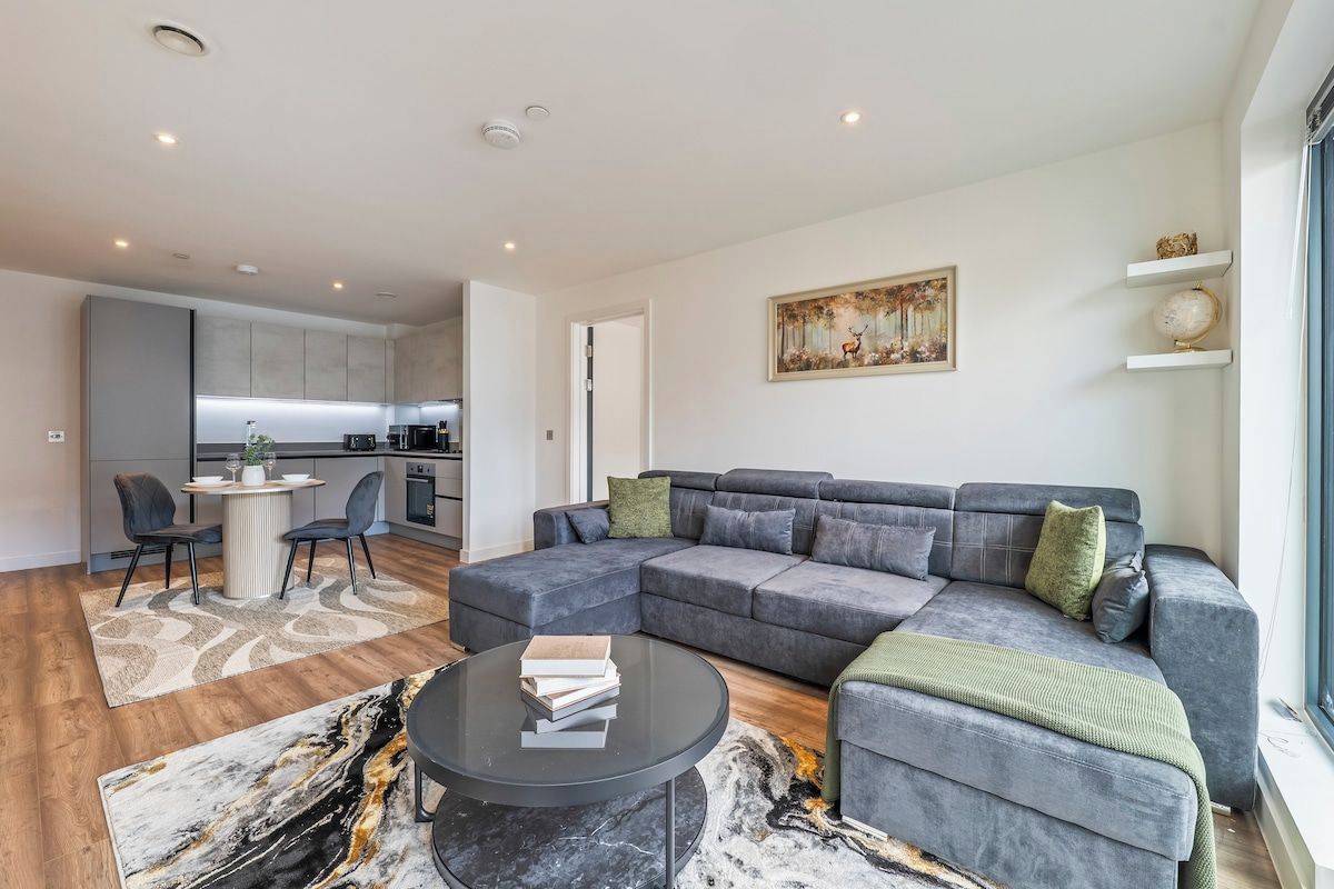 En moderne stue med en grå hjørnesofa, et sofabord og et spiseområde med stole.