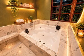 A modern bathroom with a marble bathtub, a wooden shelf with towels and plants, and a window with greenery outside. - Mansion Alameda (Quito)