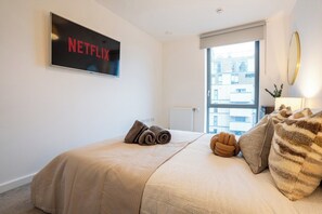 Habitación de hotel con cama, televisión montada en la pared, ventana con vistas a edificios y un radiador.