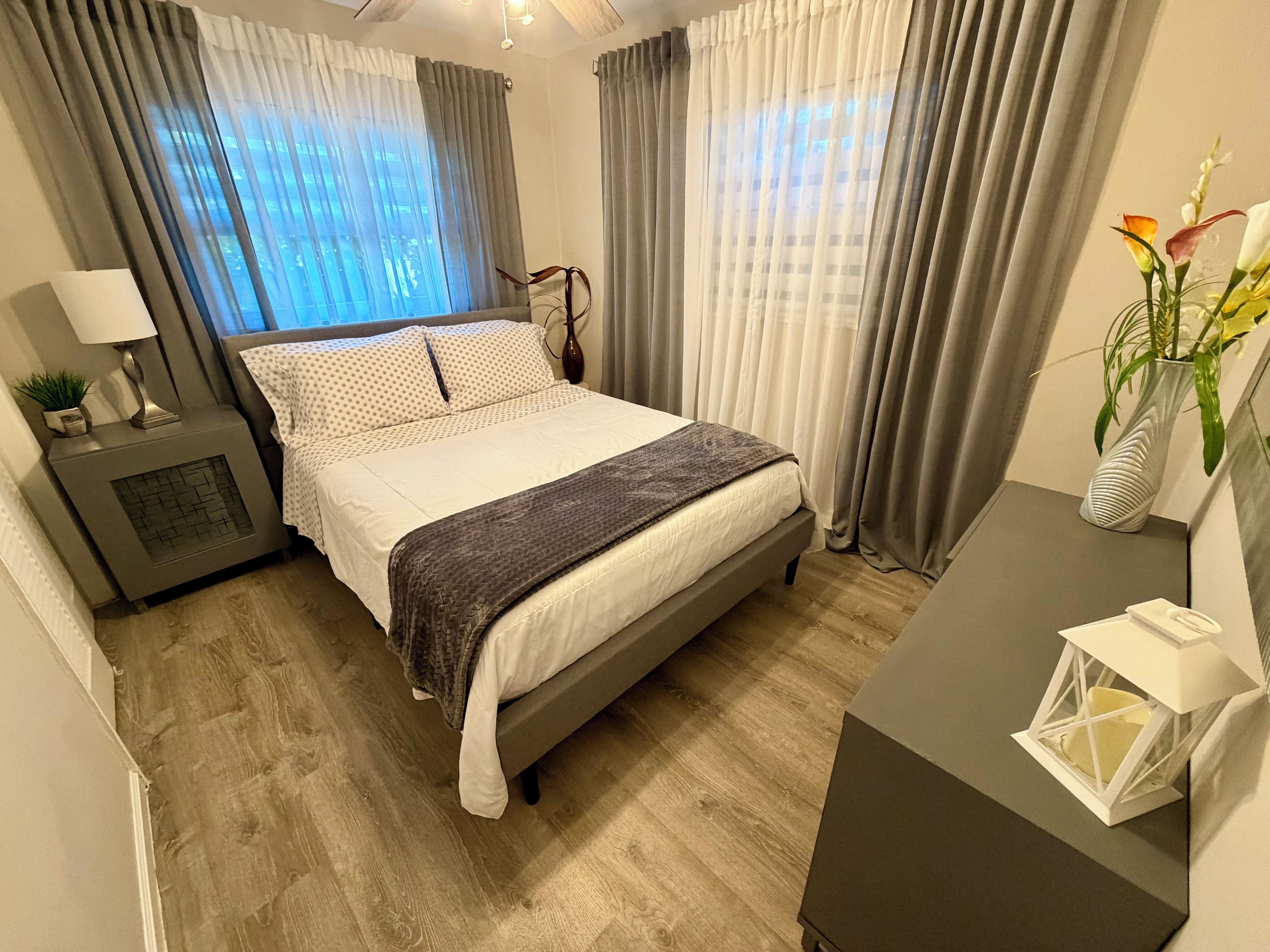 Une chambre à coucher avec un lit, une table de chevet, une lampe et des rideaux.