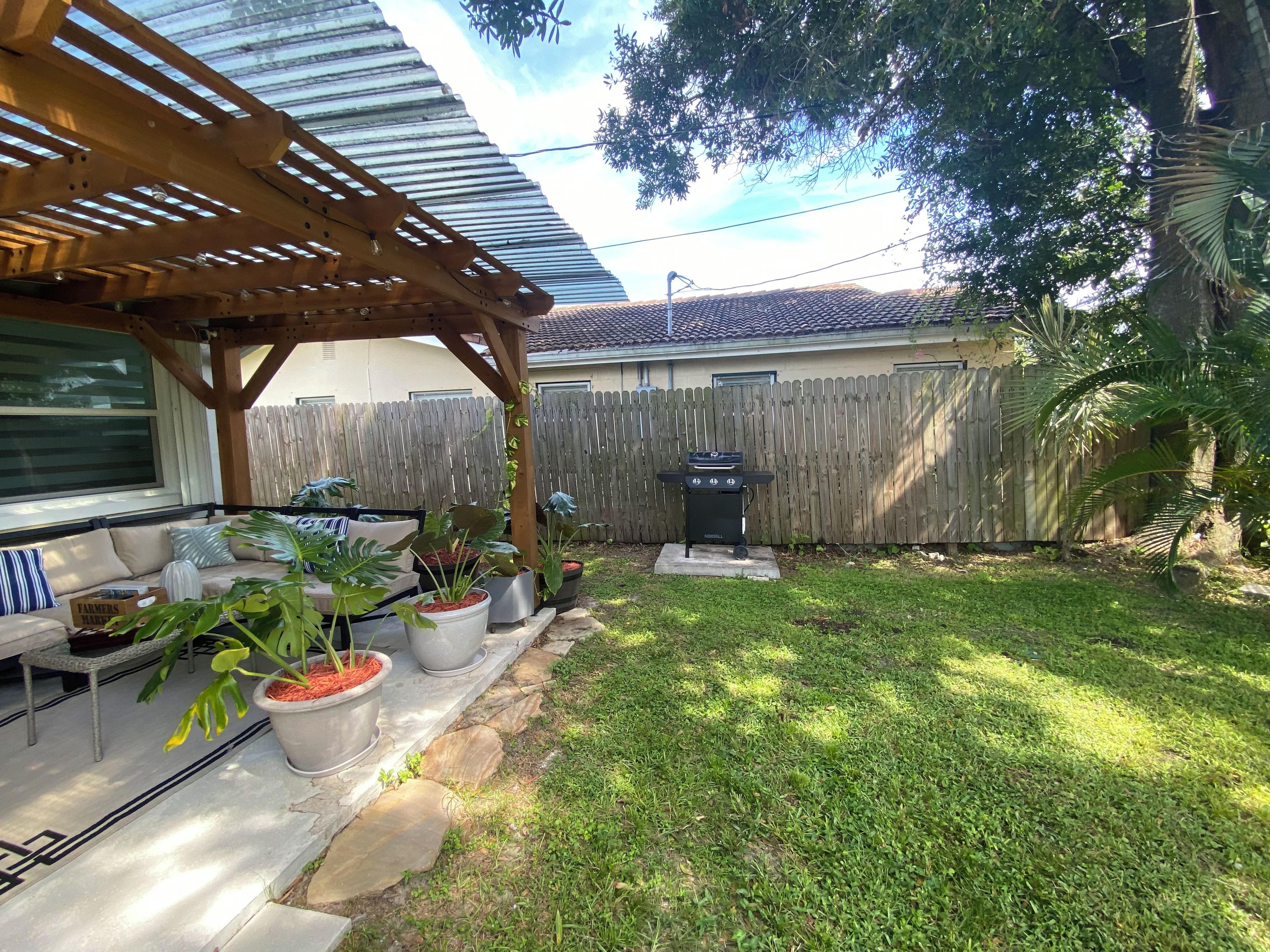 Un jardin avec une pergola en bois, un espace salon extérieur, des plantes en pot, un barbecue et une clôture en bois.