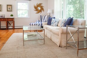 A living room with a glass coffee table, a beige sofa with blue and white pillows, a striped chair, a sun-shaped wall decoration, and a lamp. - Hollow Spring Retreat--Spacious 5bdr House (Norwalk)