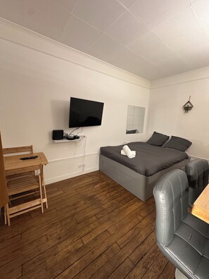 A bedroom with a bed, a TV mounted on the wall, a wooden desk, and a chair. - New Listing (Boulogne-Billancourt)