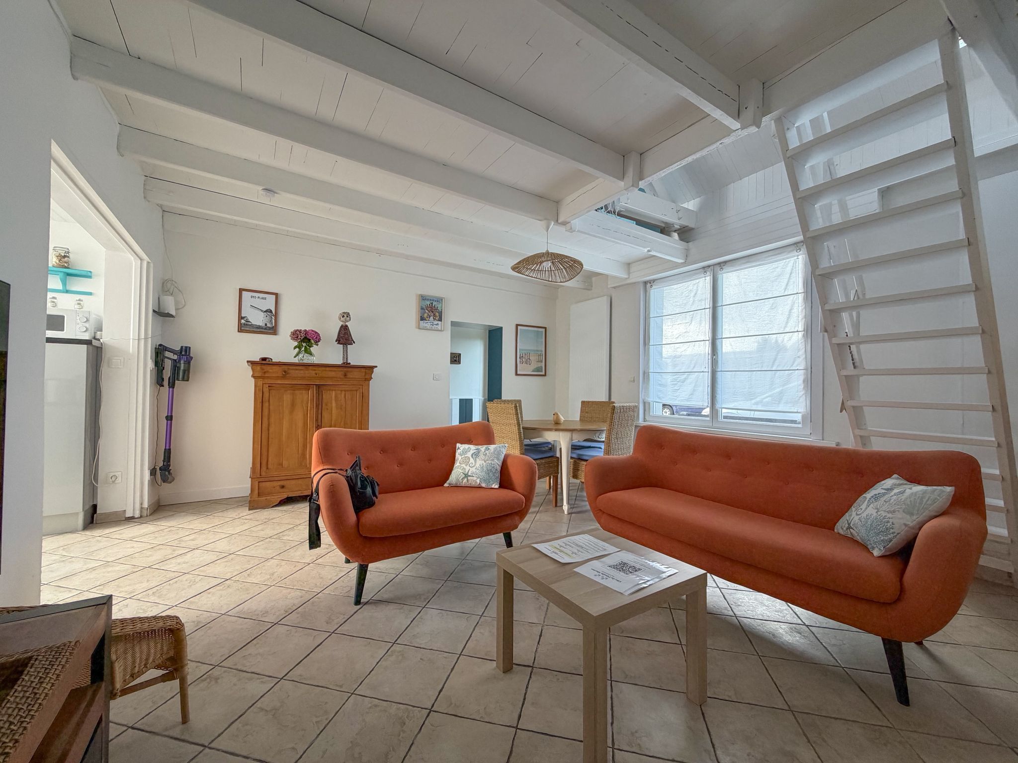 A spacious living room with two orange sofas, a wooden cabinet, and a dining area with wicker furniture.