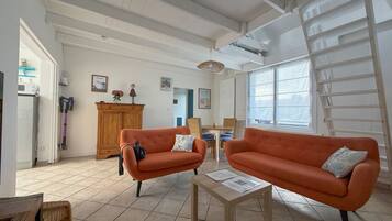 A spacious living room with two orange sofas, a wooden cabinet, and a dining area with wicker furniture.