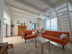 Ein geräumiges Wohnzimmer mit zwei orangefarbenen Sofas, einem Holzkabinett und einem Essbereich mit Korbmöbeln.