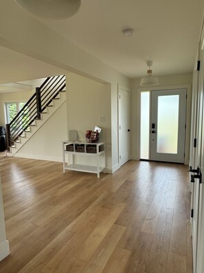 Een ruime hal met een houten vloer, een witte console tafel met manden, en een trap met zwarte leuningen.