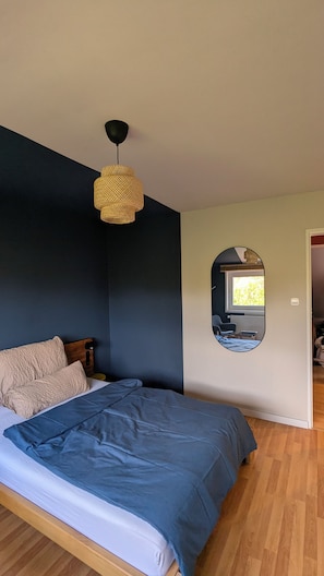 Een slaapkamer met een bed, een hanglamp, een spiegel en een houten vloer.