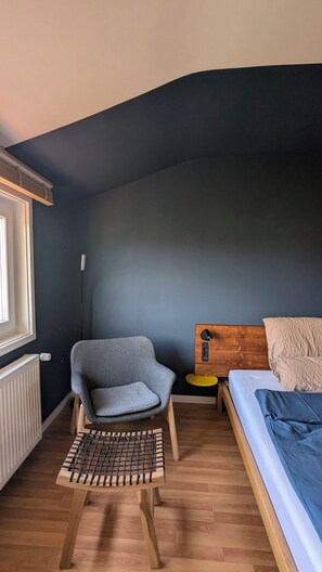 Une pièce comprenant un lit, une chaise, une petite table, un radiateur et une fenêtre.