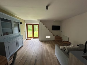 Un vaste espace de vie comprenant un escalier, un téléviseur fixé au mur et un grand meuble avec des tiroirs.
