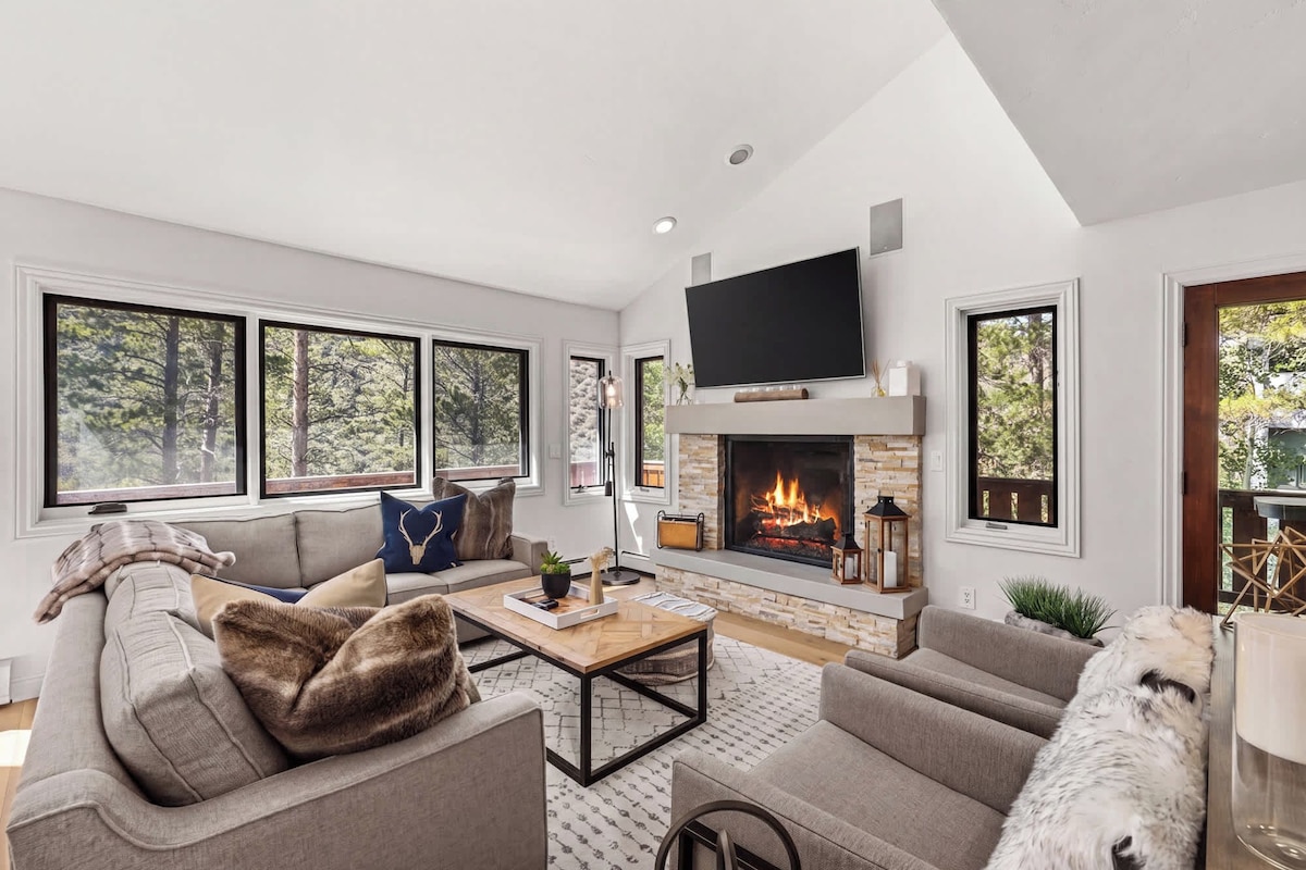A modern living room with a fireplace, large windows, and a flat-screen TV.