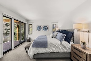 A bedroom with a large bed, a bench, a bedside table with a lamp, and a view of the outdoors through a sliding door. - West Vail Modern (Vail)