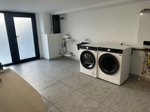 A laundry room with two front-loading washing machines, a water heater, and a small shelf with a bottle. - New Listing (Profondeville)