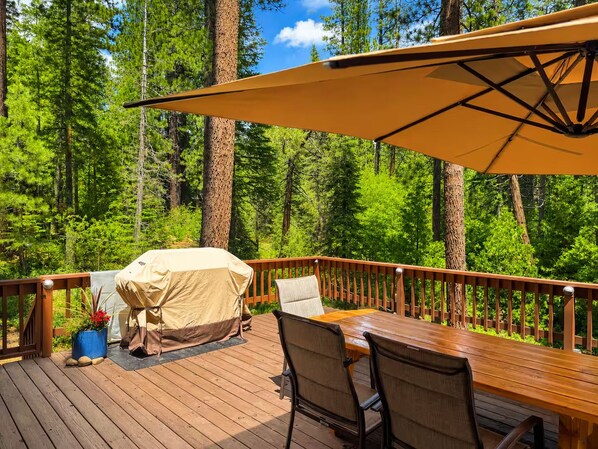 A wooden deck with a table and chairs, a covered grill, and a large umbrella.