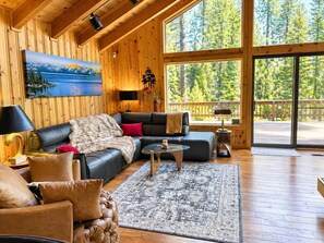 Una sala de estar acogedora con un ventanal grande, un cuadro y vistas al bosque.