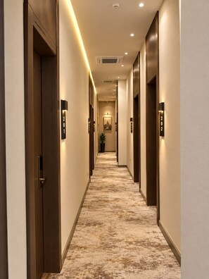 Passadís d'hotel amb sòls de moqueta, portes de fusta i indicadors numèrics il·luminats.