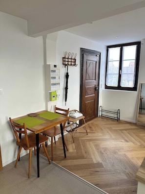 A dining area with a wooden table and chairs, a coat rack, a door, and a window with blinds. - New Listing (Bouxwiller)