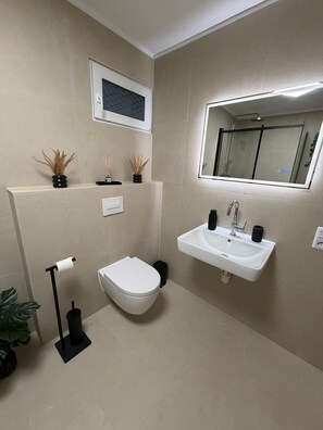 A modern bathroom with a toilet, sink, and a shower area. - New Listing (Marienheide)