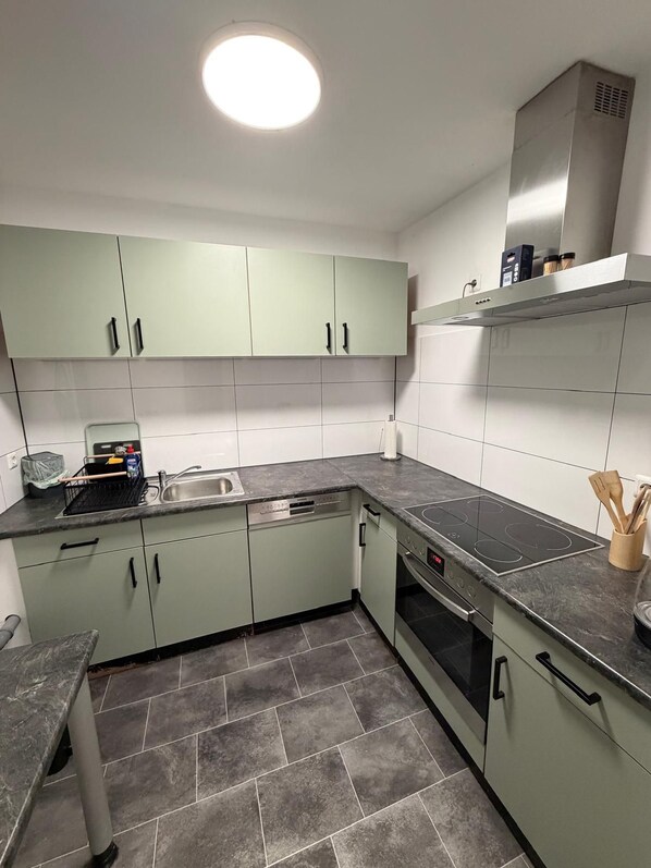 A modern kitchen with light green cabinets, a stainless steel sink, a dishwasher, and a built-in oven. - New Listing (Marienheide)