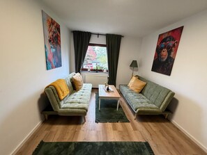 A living room with two green sofas, a coffee table, a radiator, and a window with curtains. - New Listing (Marienheide)