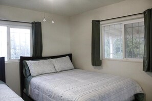 Quarto com uma cama de solteiro, janela com cortinas e luminária suspensa.