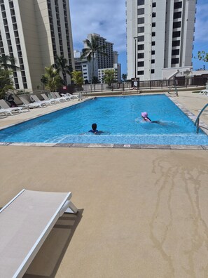 Une piscine entourée d’immeubles imposants, avec des chaises longues et des palmiers.