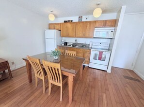 Une cuisine de taille réduite avec des meubles en bois, une table à manger en verre et un réfrigérateur blanc.