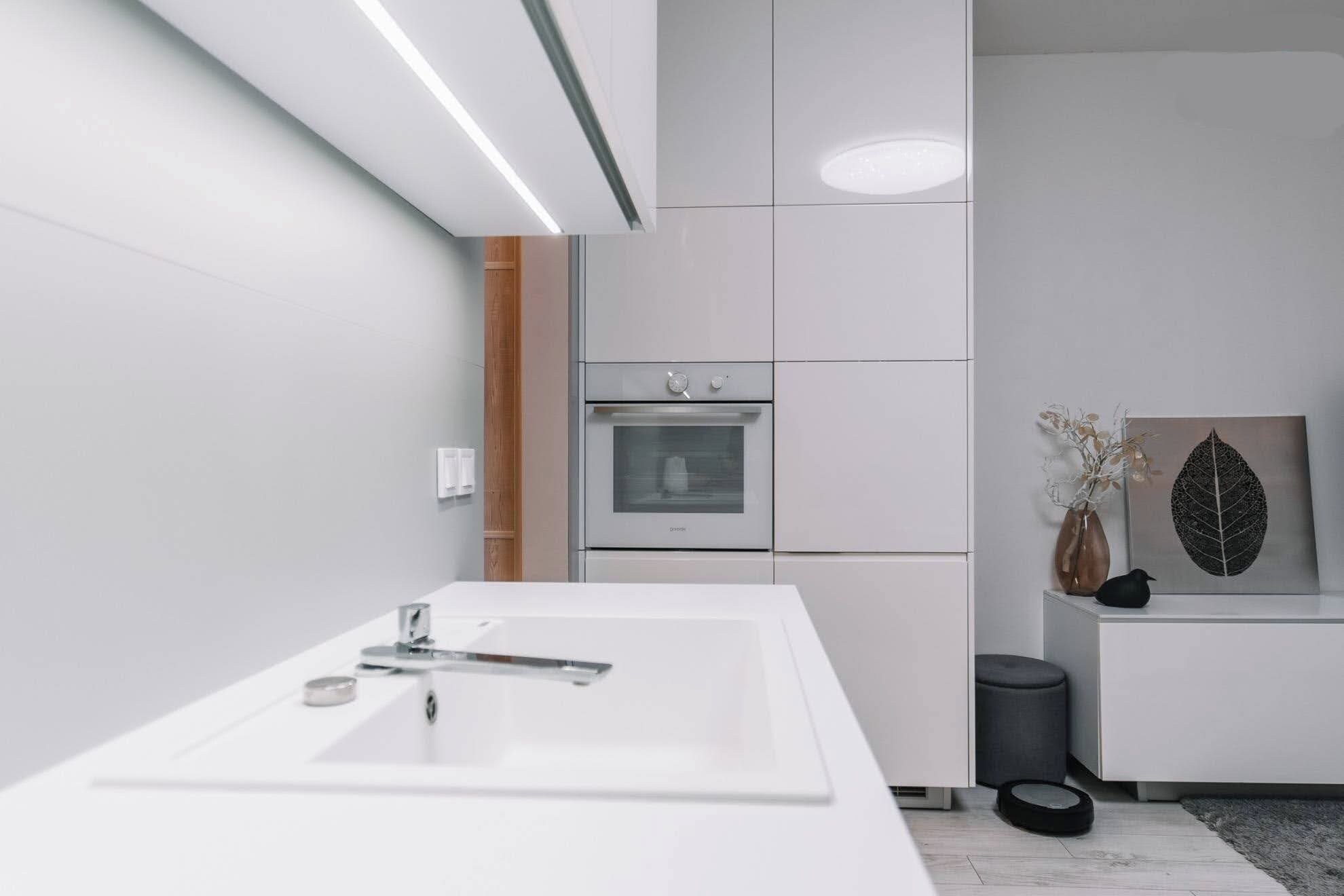 A modern bathroom with a white sink, a built-in oven, and a grey trash bin.
