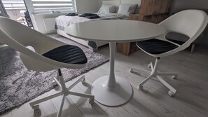 Une chambre moderne avec une table ronde et deux chaises, un lit avec une couette grise et un tapis gris.