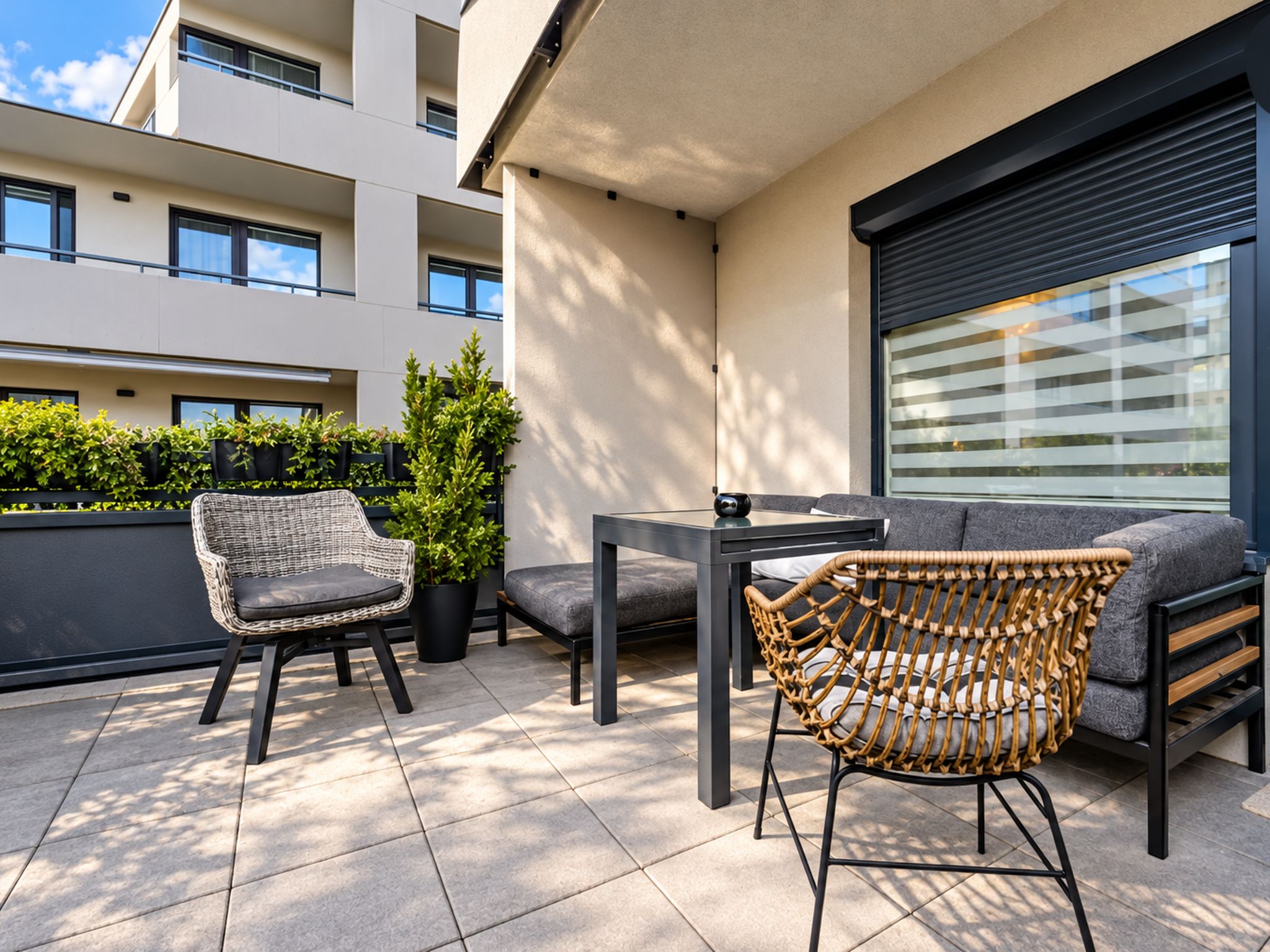 An outdoor balcony with a seating area, including a wicker chair, a sofa, and a table.