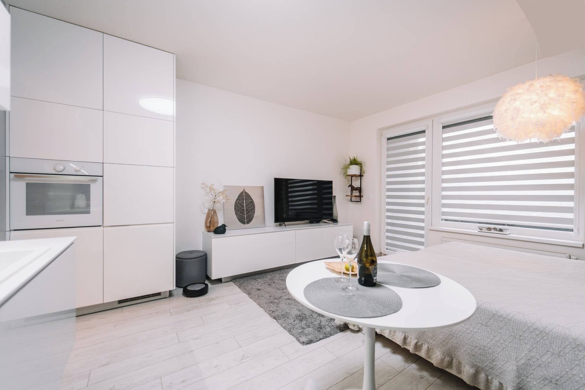 A modern kitchen with white cabinetry, a built-in oven, and a dining area with a round table and a hanging light fixture.