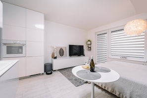 Une cuisine moderne avec des meubles blancs, un four encastré et un coin repas comprenant une table ronde et un luminaire suspendu.