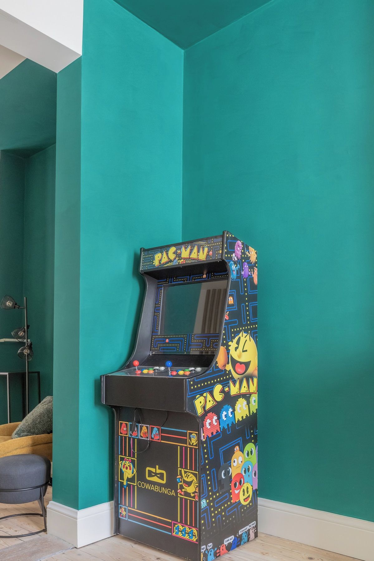 Pac-Man-peliautomaatti turkoosinsinisellä seinällä varustetussa huoneessa.