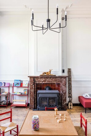 Una habitación con chimenea, un candelabro, un sofá rojo y una mesa de madera con un tarro de cuentas de colores.