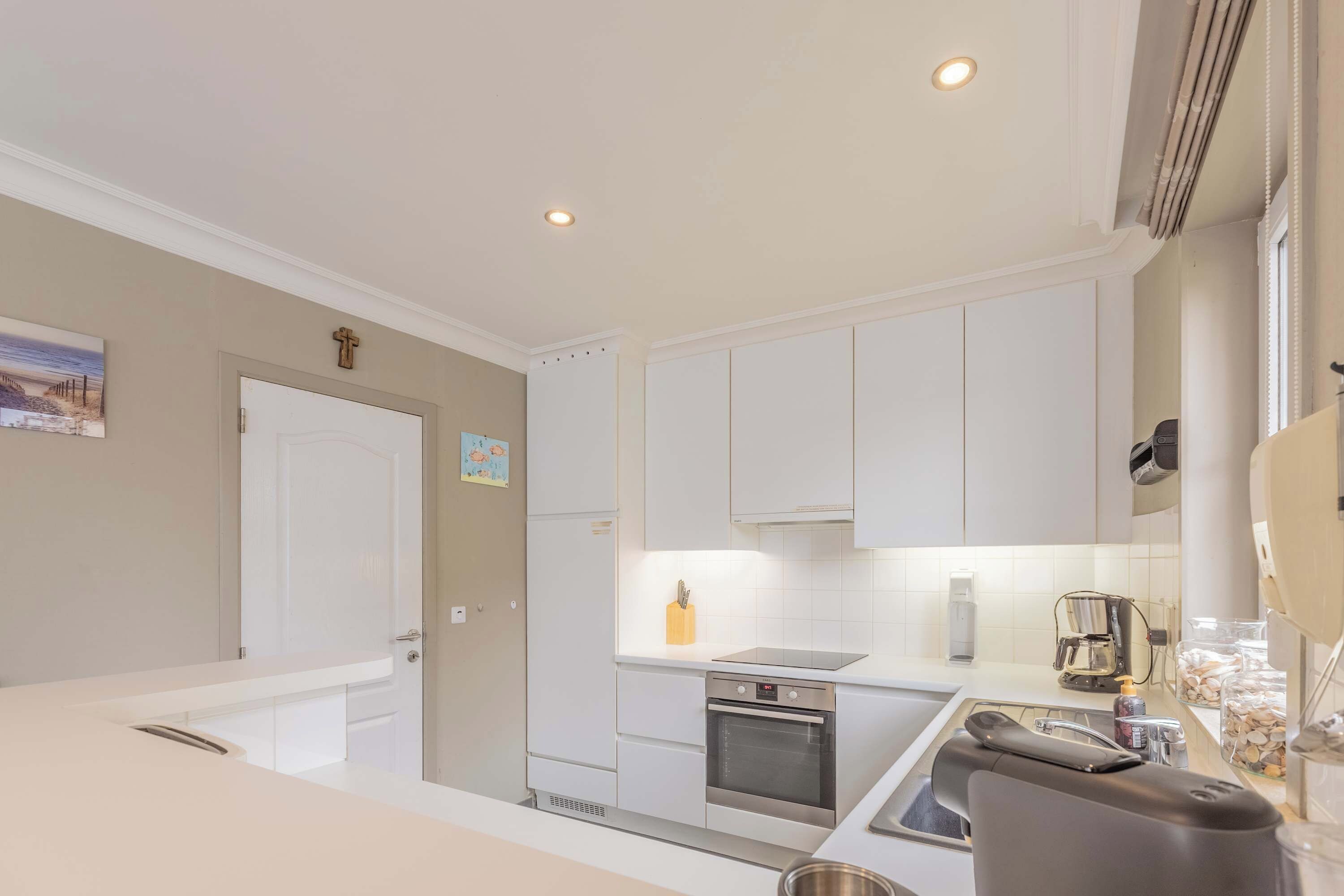 A modern kitchen with white cabinets, a built-in oven, and a stainless steel sink.