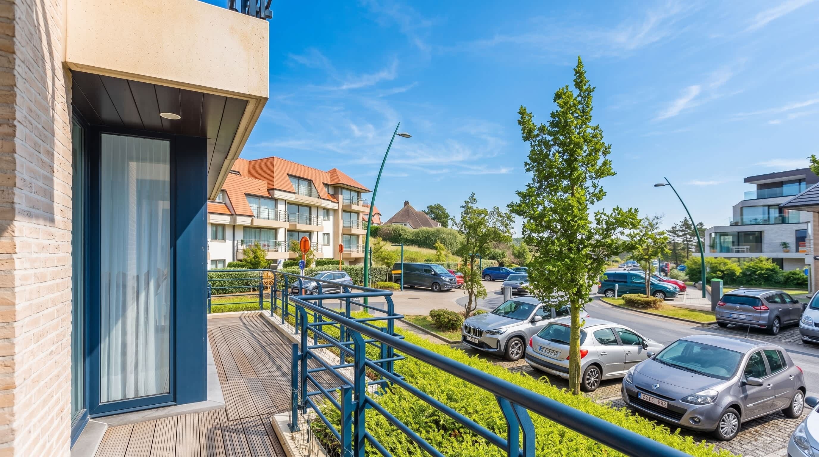 Een woongebouw met een balkon, een parkeerplaats met auto's en een heldere lucht.