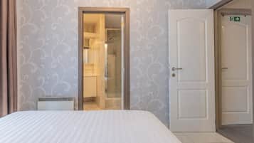 Een hotelkamer met een bed, een badkamer met douche en een deur met een nooduitgangsbordje.